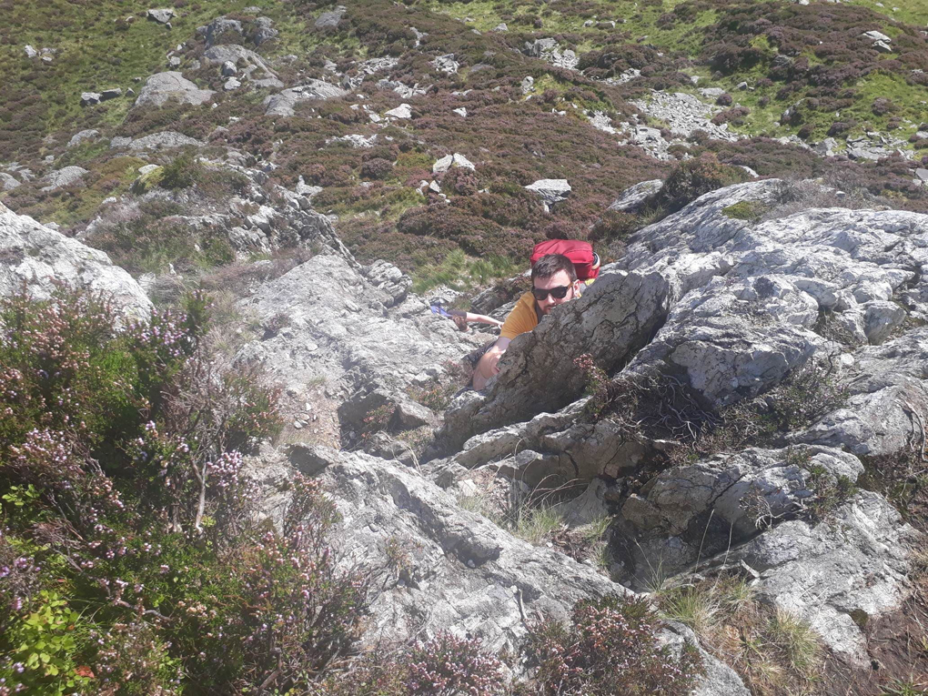 A shot of the mountains with a guy peeping round some rock he is climbing below.