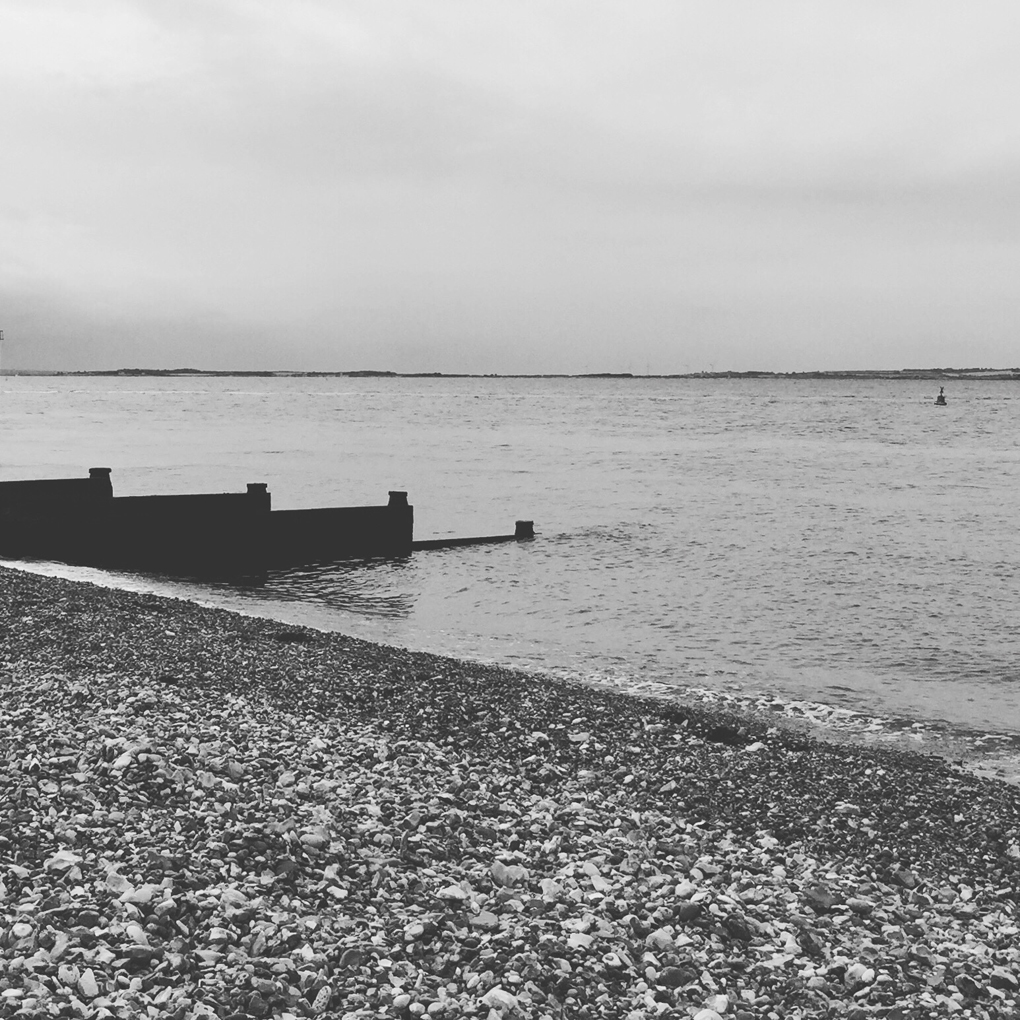 A rocky beach with a groyne, the sea, and more land in the far distance