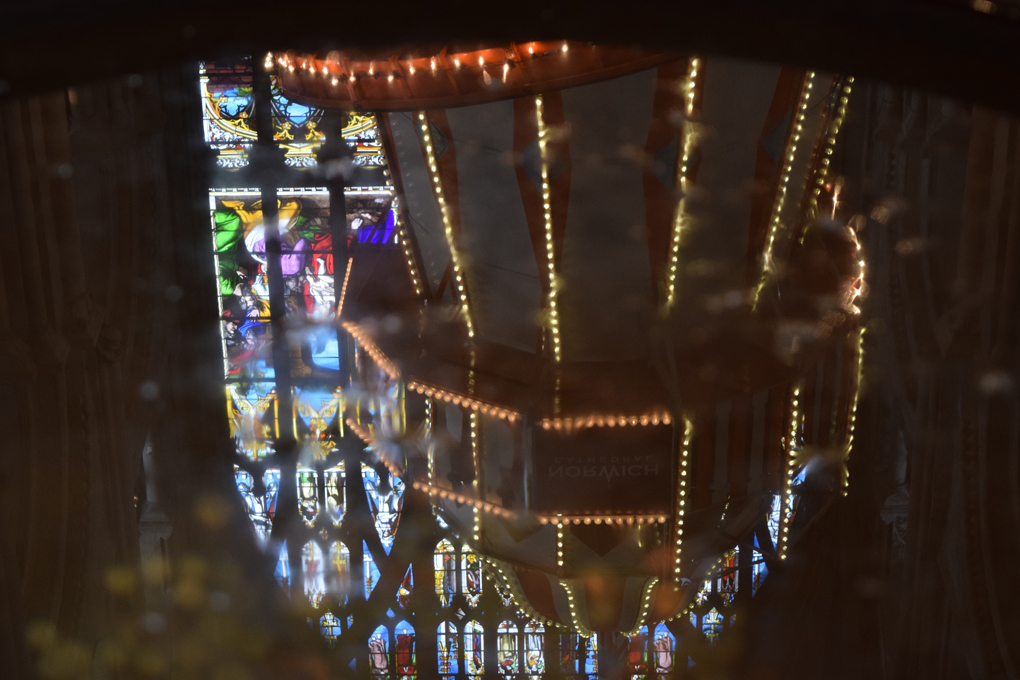 The reflection of a helter skelter in the water of a baptismal font with coins in the bottom.