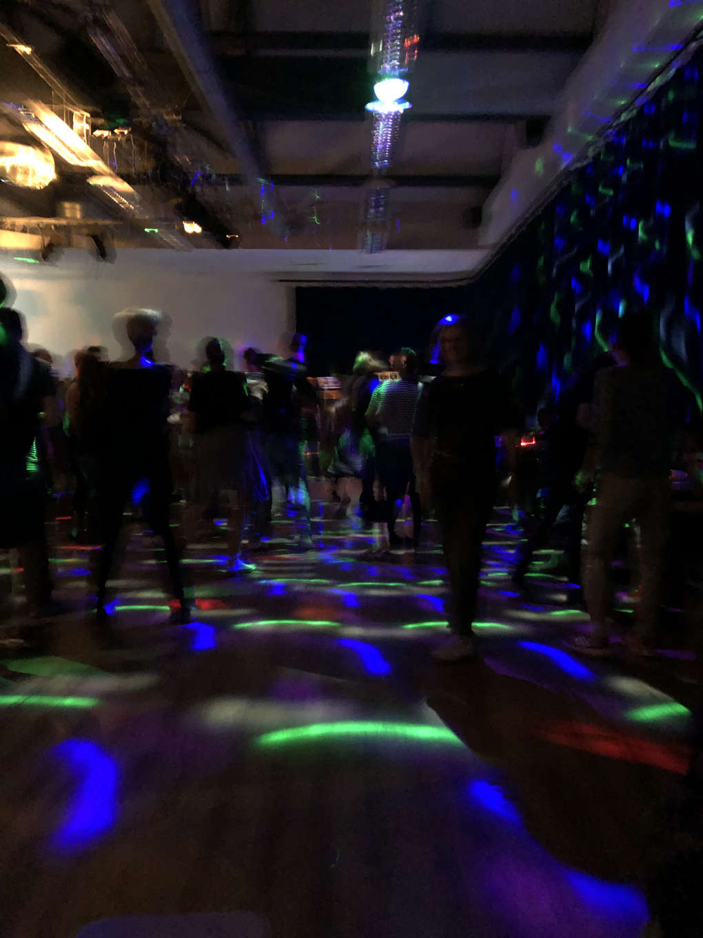 Lots of middle aged people jumping around in room lit with psychedelic lights