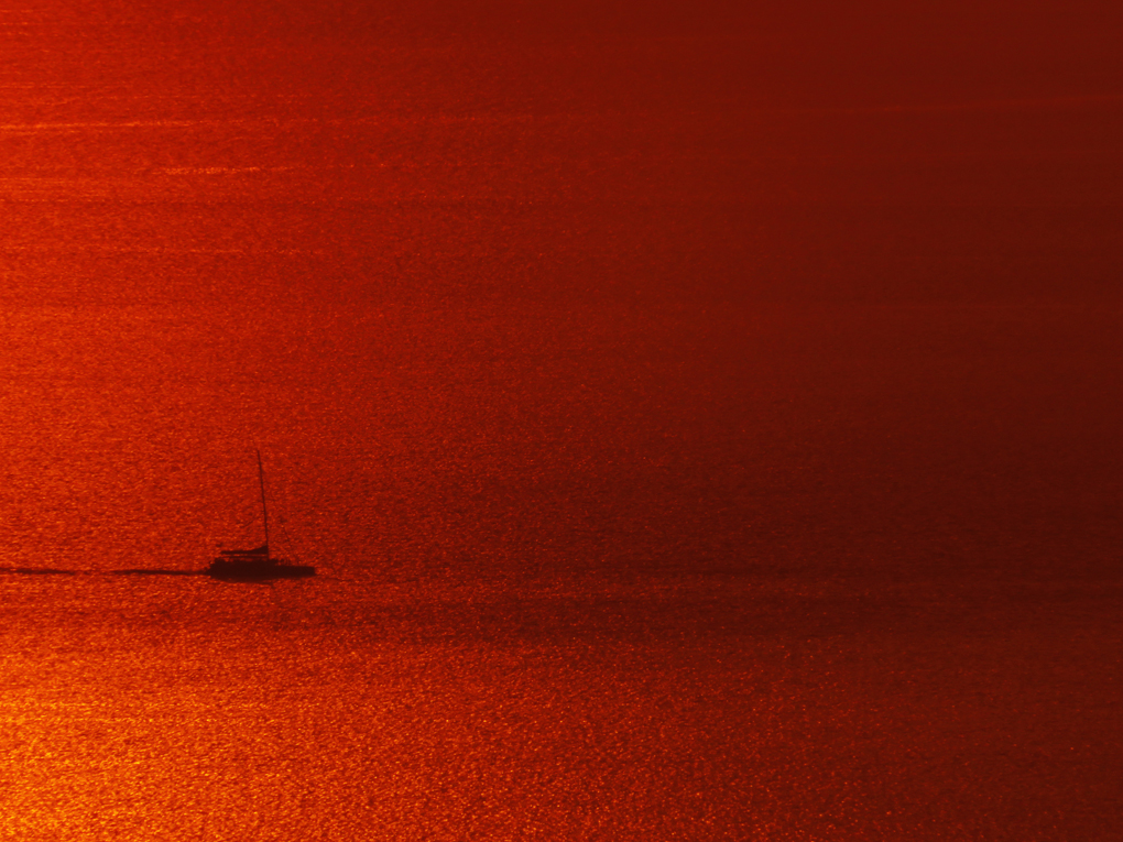 A sailing boat is captured in the golden glow of a Santorini sunset