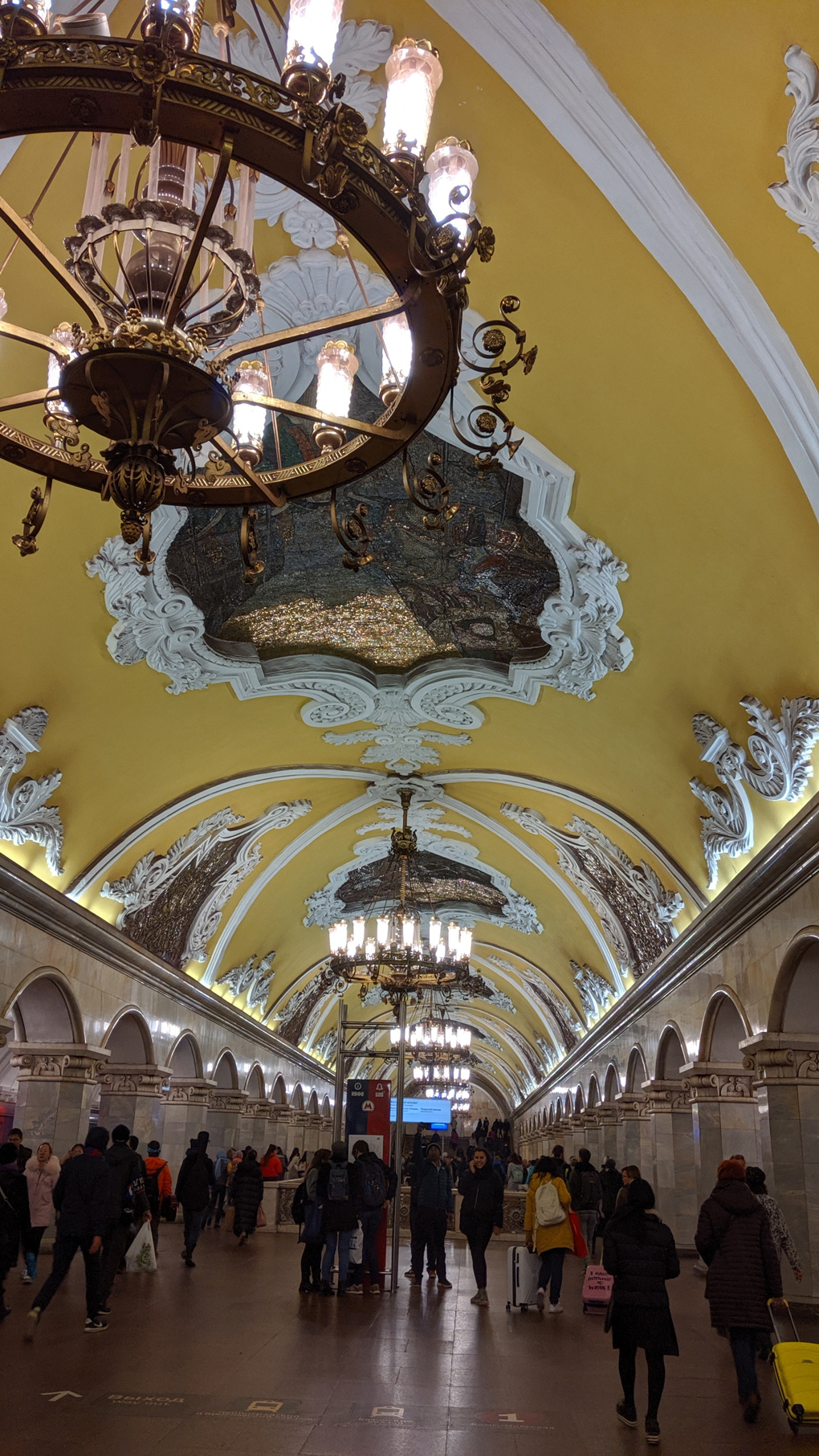 A tube station with bright yellow Walla, mosaics and chandeliers.