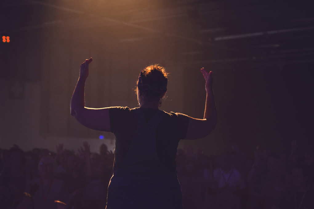 A sign language interpreter in full, expressive flow under warm stage lighting in front of a crowd of thousands.