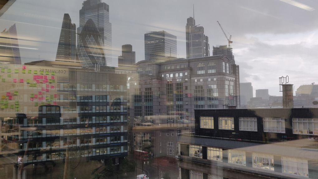 Reflections of bright post-it notes and whiteboards inside the building contrast with the dramatic grey London buildings outside.