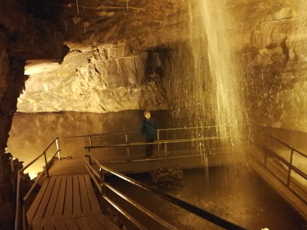 waterfall in a cave with path leading behind it, with lady looking into waterfall