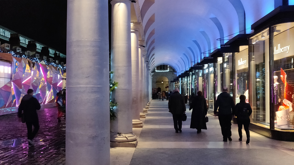 People walking in the brightly lit colonnade outside the Royal Opera House late at night