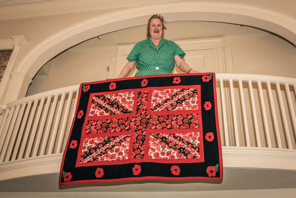 Lady in forties costume on balcony with commemoration poppy wall hanging