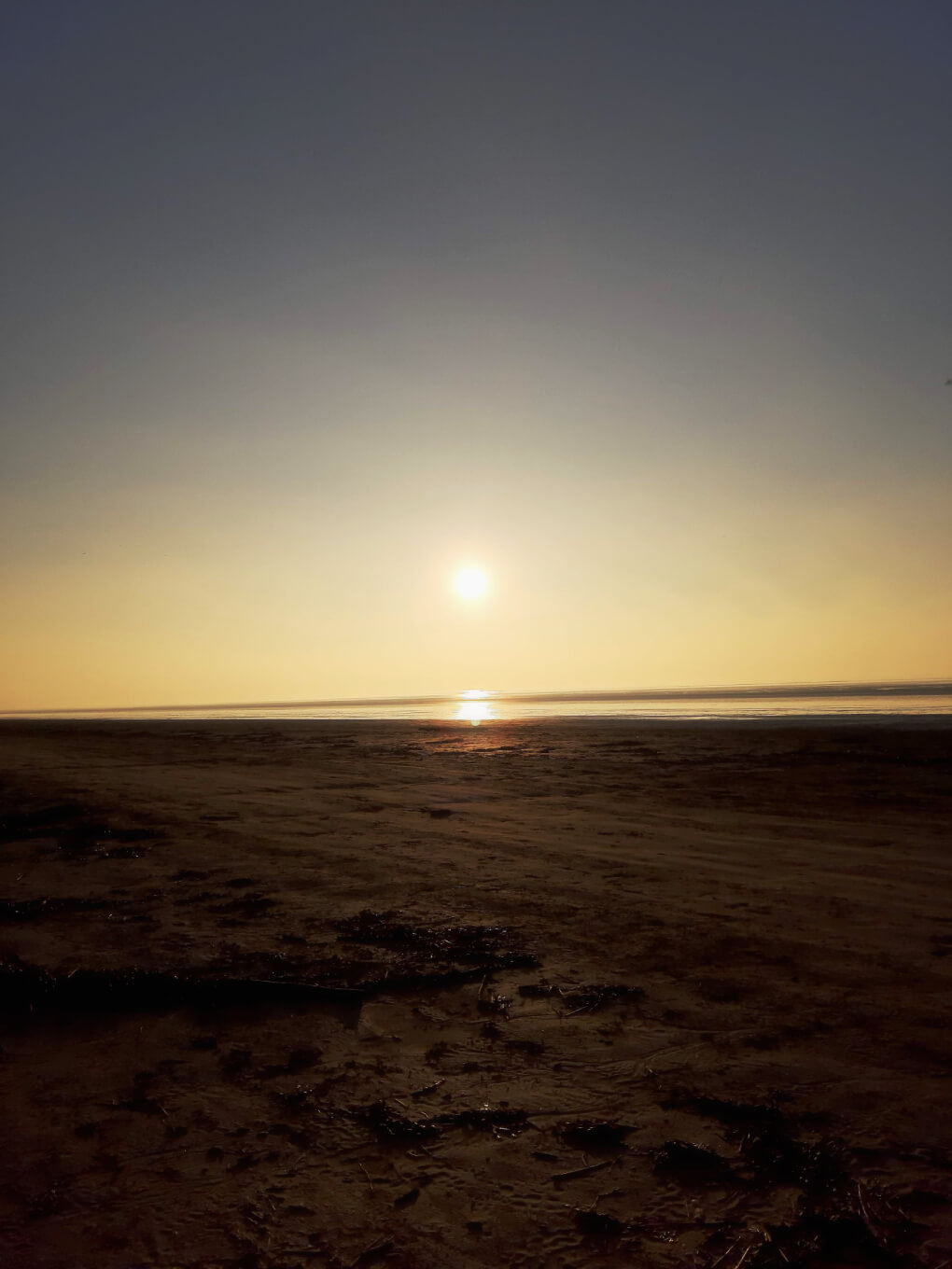 Bright sun descending towards a wet, sandy beach
