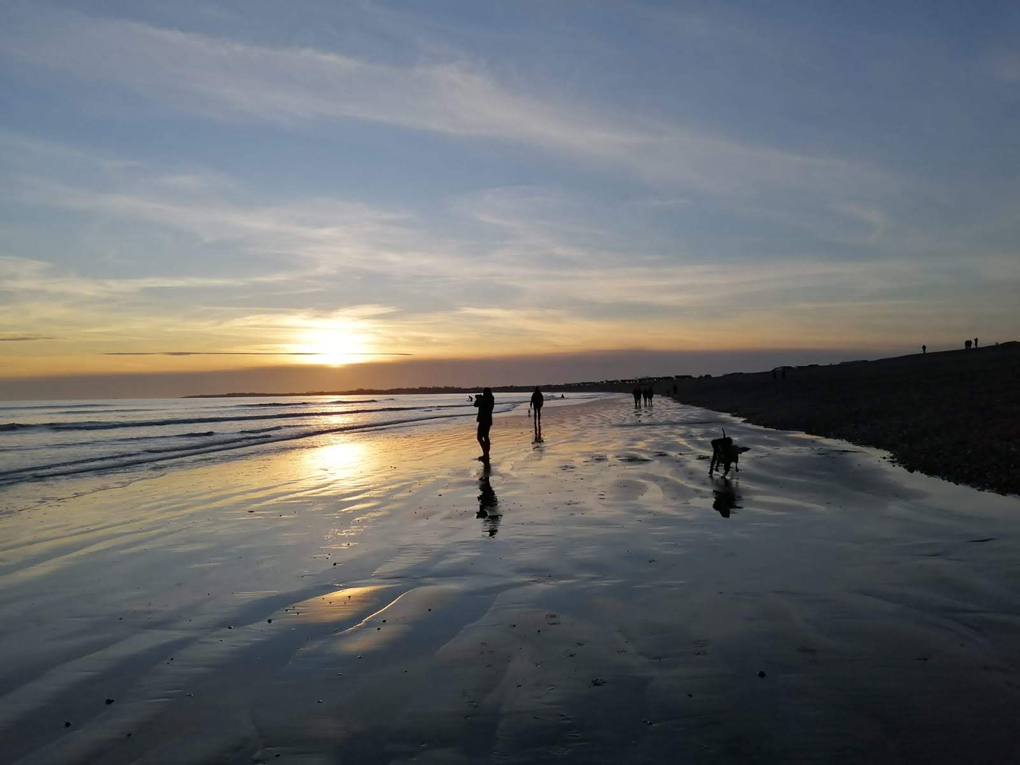 The setting sun is reflected on the calm sea and sand of this almost deserted beach