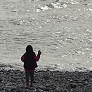 Small human throws stones into big ocean