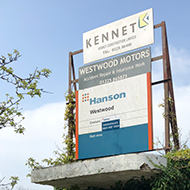 A doorway overgrown with vegetation. Above the door there are a number of worn signs for old automotive businesses.