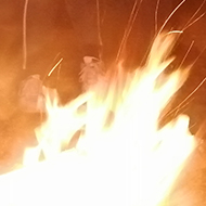 Family gathered at dusk around a fire. Jon has large poking stick.