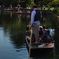 Punting boats on the river Stour in Canterbury by a park with Marlowe Theater in the background.