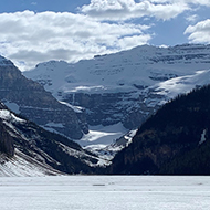 A frozen lake in the foreground with a snow capped mountain range behind