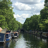 Avon and Kennet canal stretching into the distance with narrow boats moored to either side and sunlight shining off of emerald water