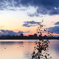 Sun setting over water with a silhouette of buildings in the distance.