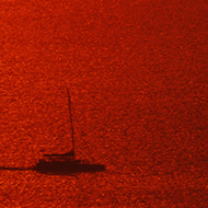 A sailing boat is captured in the golden glow of a Santorini sunset