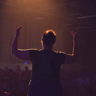 A sign language interpreter in full, expressive flow under warm stage lighting in front of a crowd of thousands.