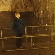 waterfall in a cave with path leading behind it, with lady looking into waterfall