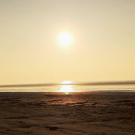 Bright sun descending towards a wet, sandy beach