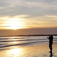 The setting sun is reflected on the calm sea and sand of this almost deserted beach