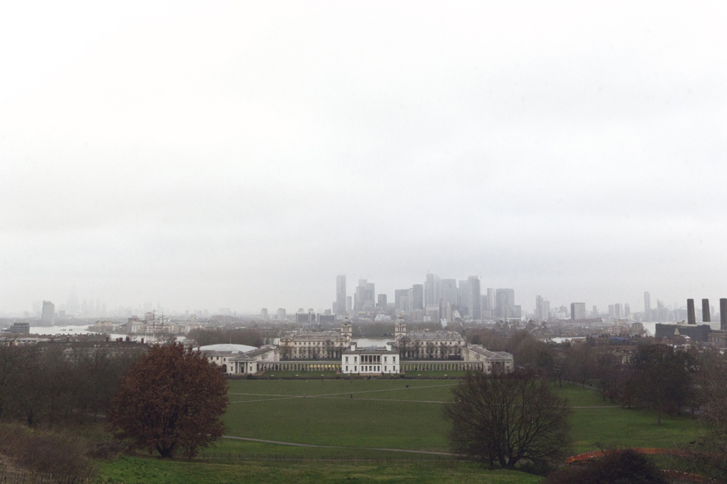 Photograph overlooking the historic buildings and university in Greenwich with London shrouded by fog in the distance.