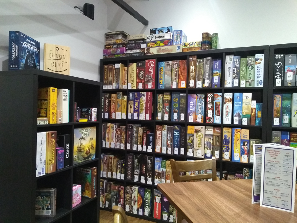 The corner of a room filled with shelves of many different board games, chair and table with menu on.
