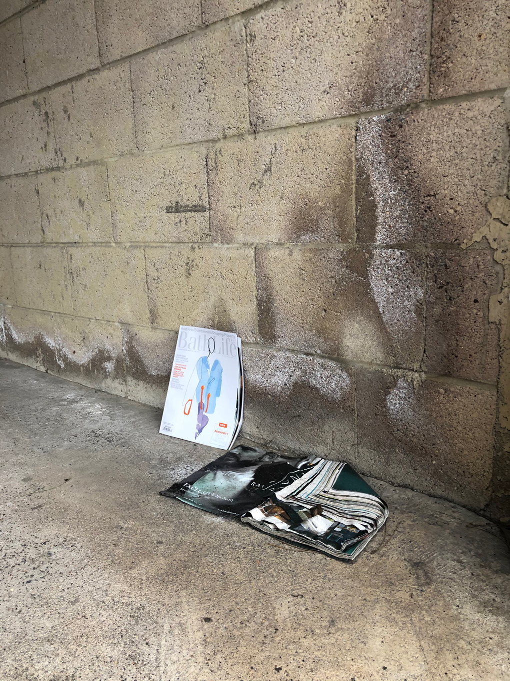 Two dog-eared, water damaged magazines on the floor of an empty garage