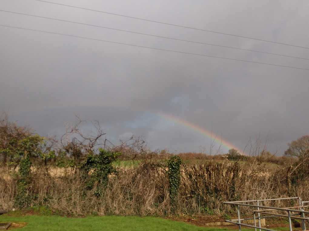 Rainbow against a back drop of dark grey clouds and green fields