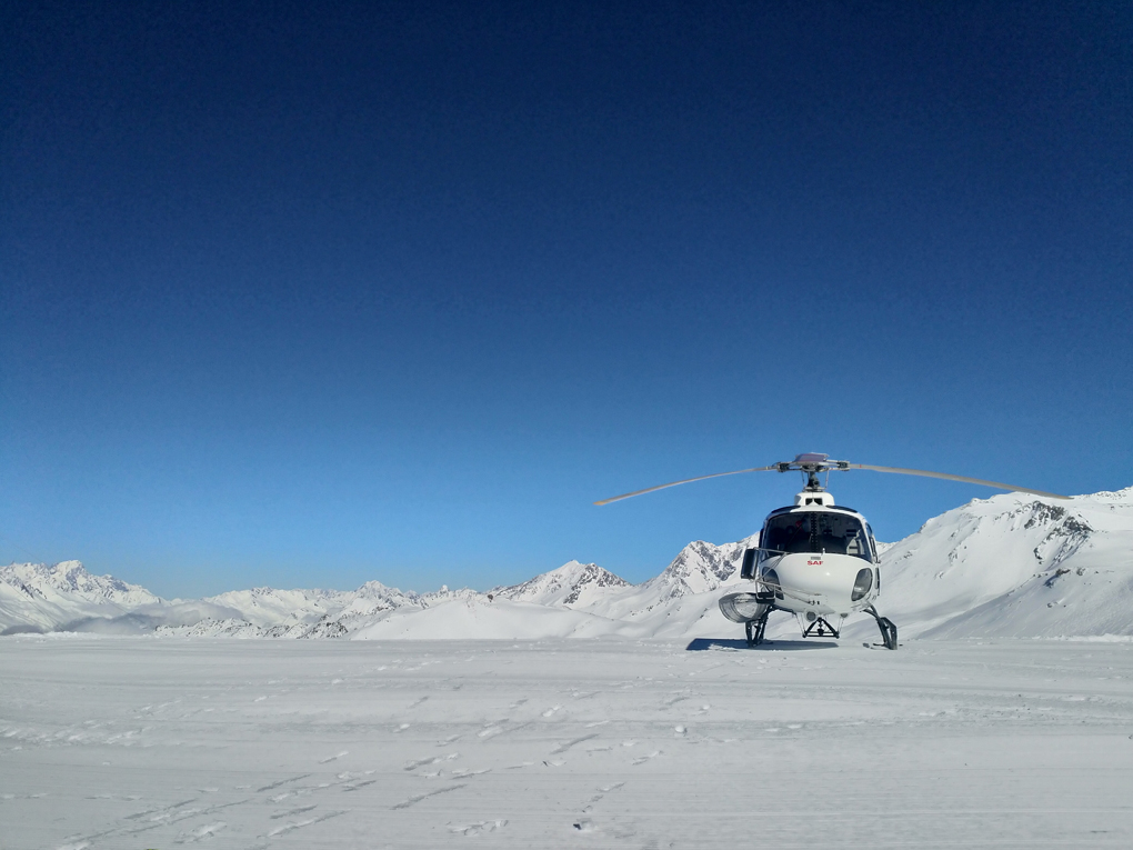 A white helicopter parked on pristine snow with empty blue skies behind it.