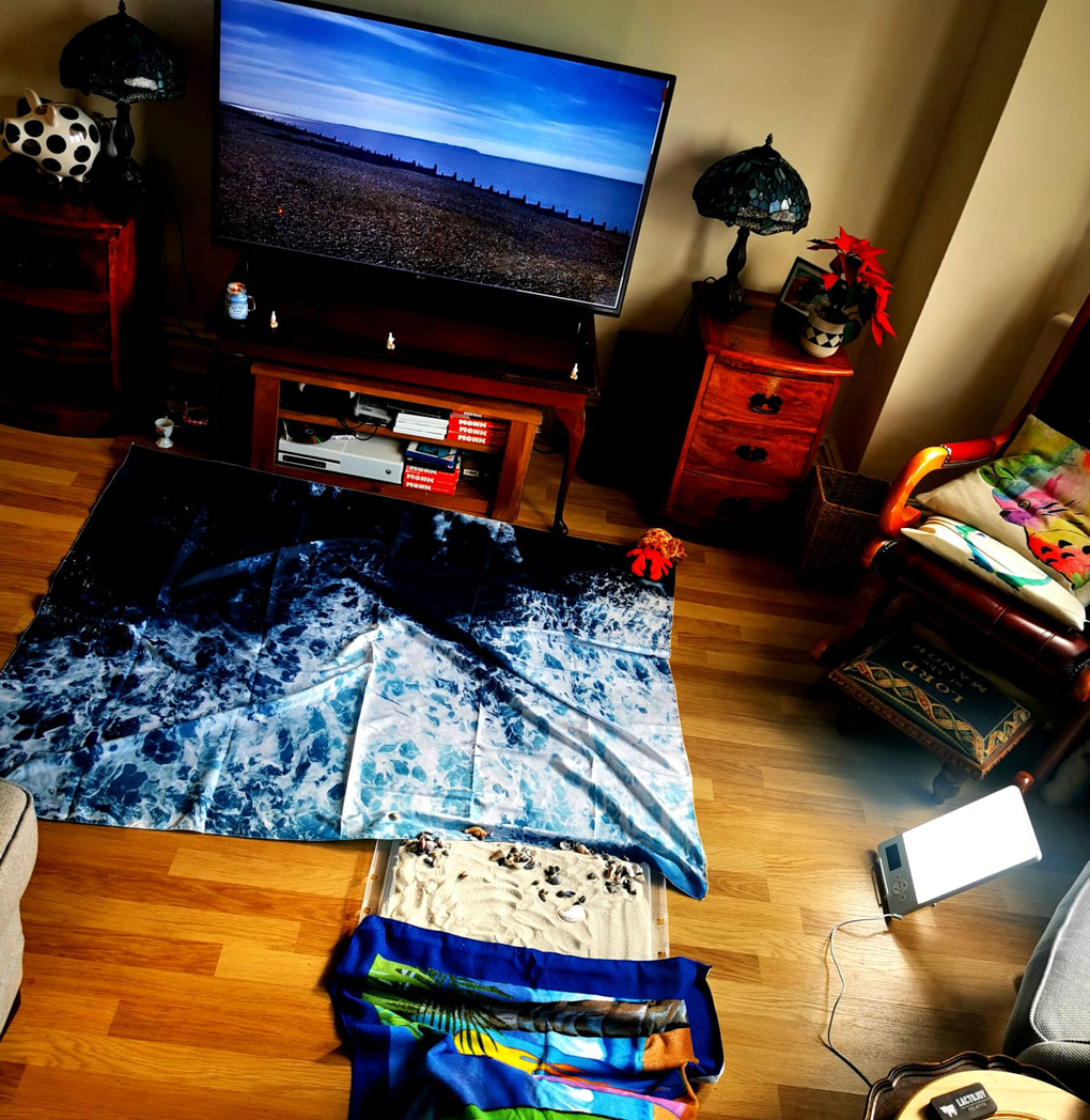 sandpit and cloth looking like water in front of a TV picture of the sea