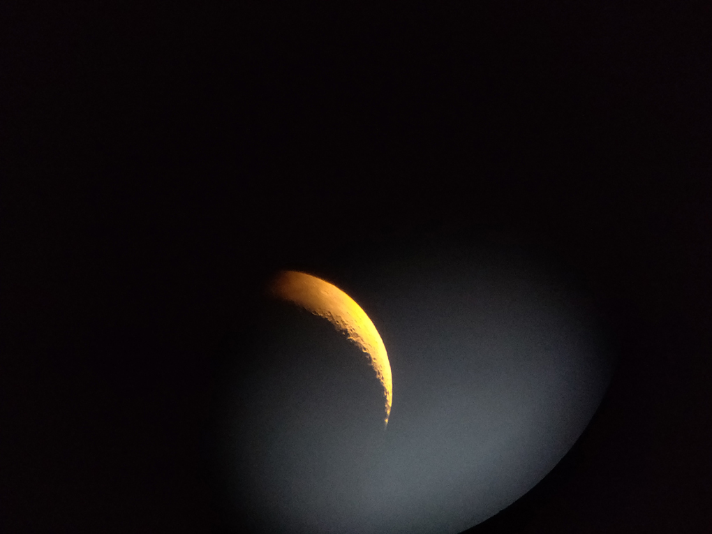 A hazy crescent moon viewed through a telescope