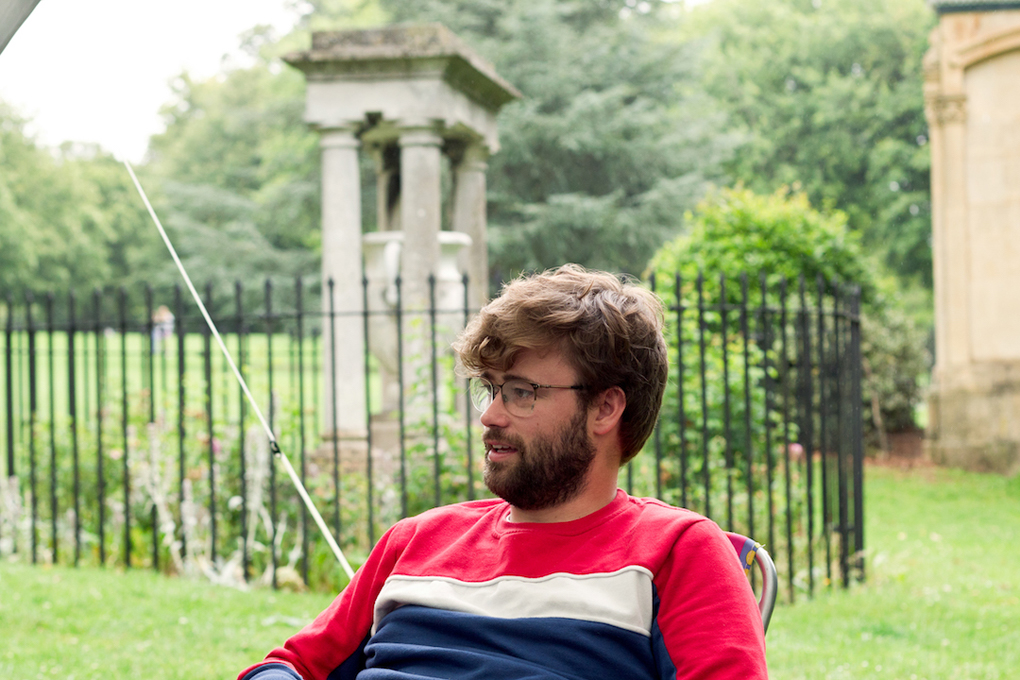 Young man in red and blue sat under a gazebo talking.