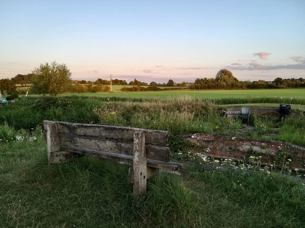 A bench by the canal with a view of fields