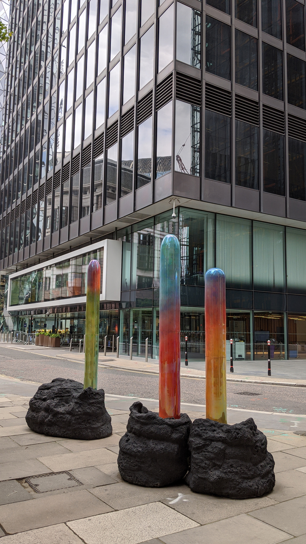 Three coloured shafts eminating from large black stones, outside an office building in central London.