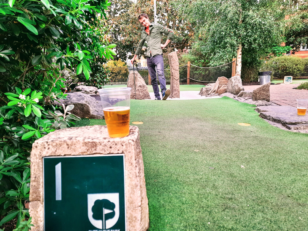 A shot down the green of a mini golf course with the hole number visible and a plastic cup of beer balanced on top.