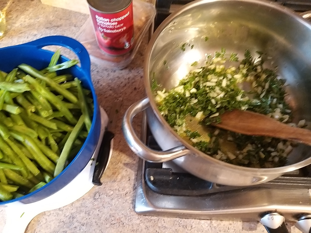 Chopped onions and parsley sizzling in a pot and prepared runner beans waiting on the side to join them.