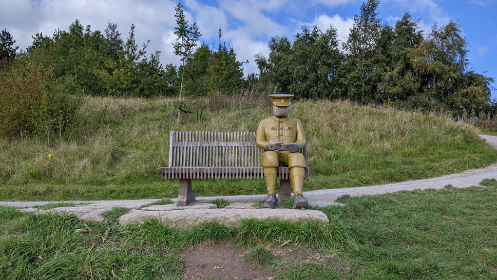 Bench with a life-size wooden figure of a soldier sitting at one end.