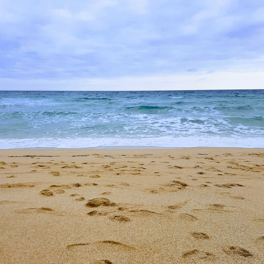 Horizontal bands of yellow sand, crashing waves, blue seas, and a vibrant blue sky