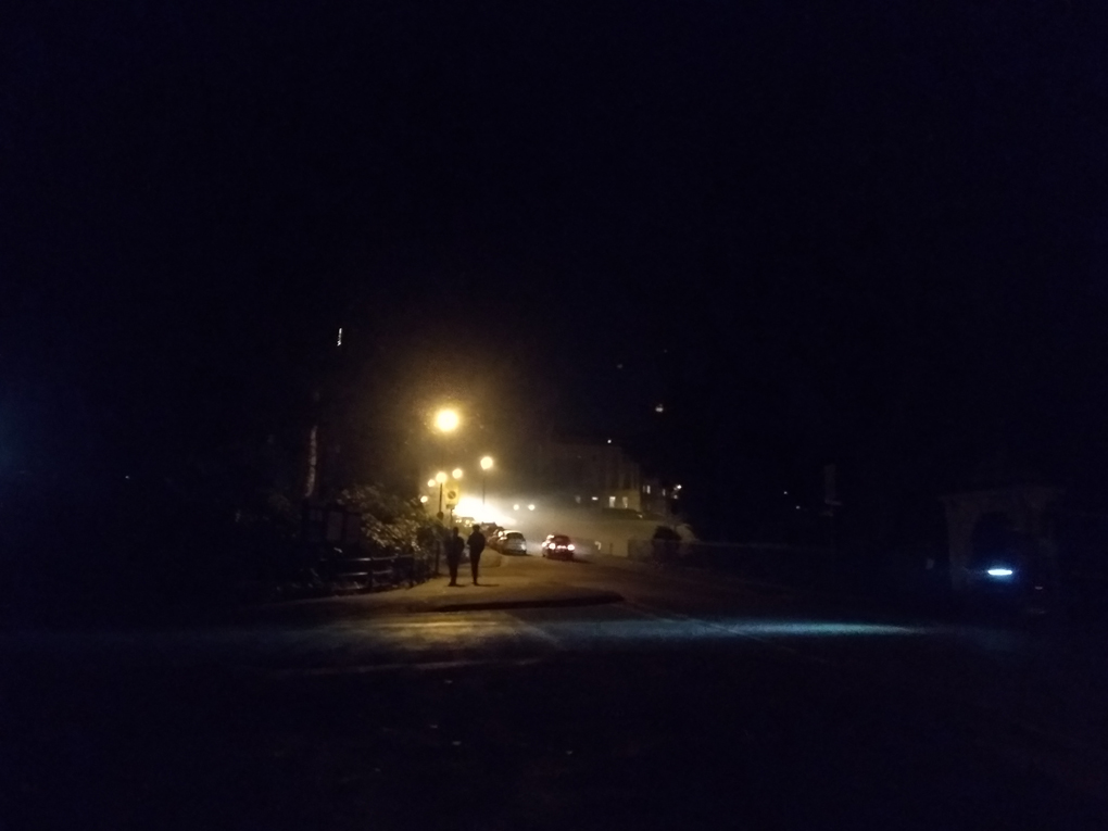 Darkness and fog illuminated by street lamps on a road going uphill away from you