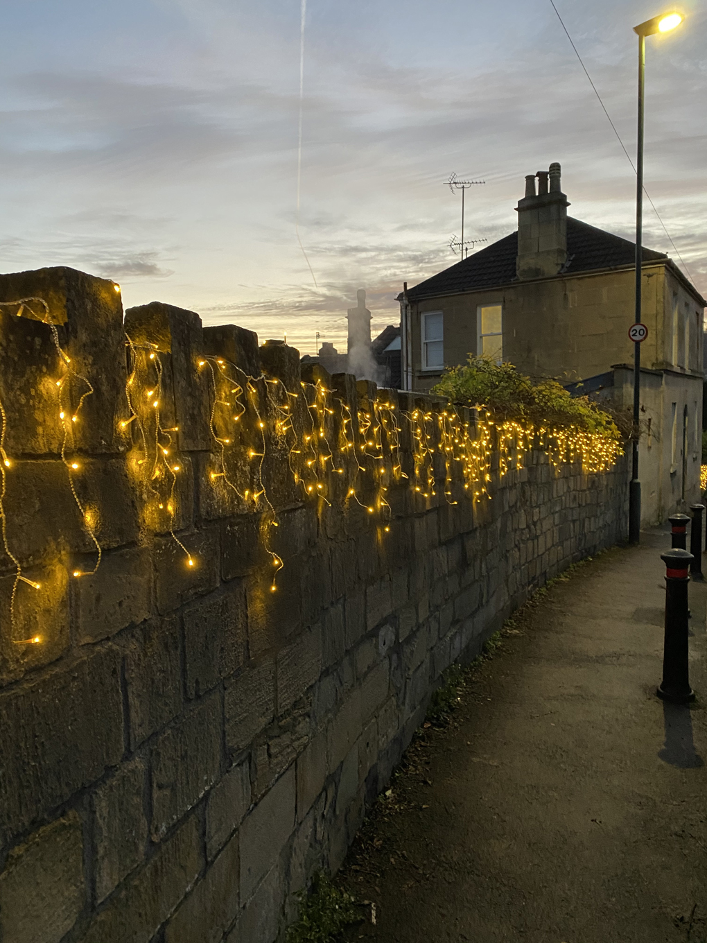 A stone wall alongside a road covered in small lights. The lights give off a warm glow.