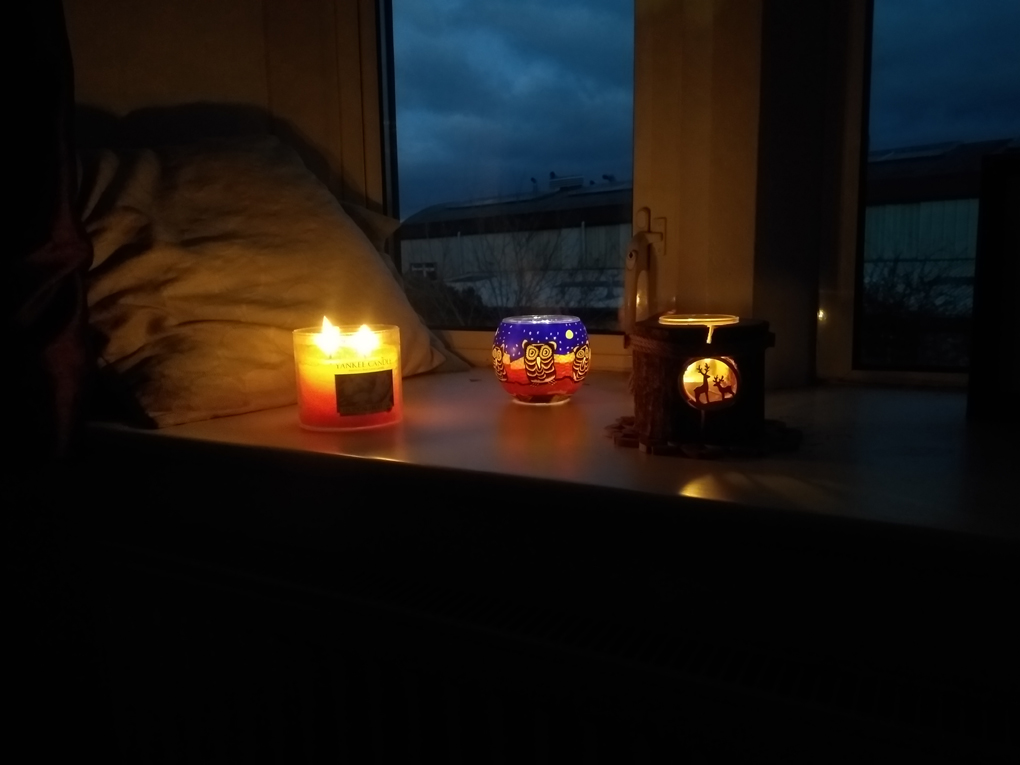 Three candles of different types on a windowsill, tree trunk deer, owl jar and scented candle