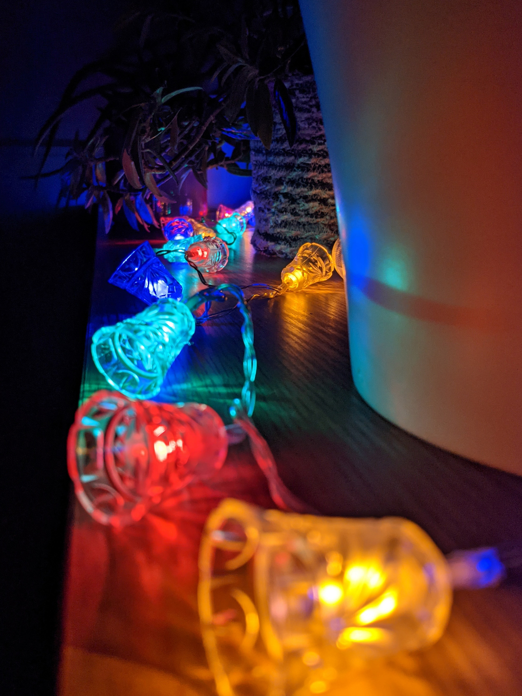 Different coloured Christmas fairy lights, shaped like church bells, laid along a reflective cabinet worktop