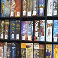 The corner of a room filled with shelves of many different board games, chair and table with menu on.