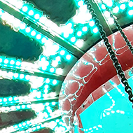 Bright lights in the canopy over a rotating swing ride, with chains to each seat hanging down into the picture