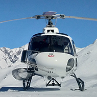 A white helicopter parked on pristine snow with empty blue skies behind it.