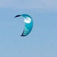 It shows kite surfers on the shallow wavey beach with blue sky and wispy clouds above