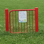 A red metal gate standing in the middle of a green field