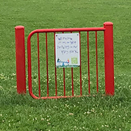 A red metal gate standing in the middle of a green field