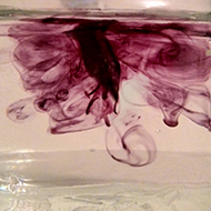 A fountain pen nib dipped in water with bright ink swirling around it